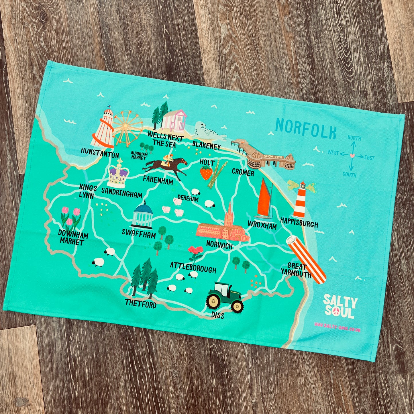 Map of the North Norfolk area on a teal tea towel with 'Salty Soul' branding, placed on a wooden surface.