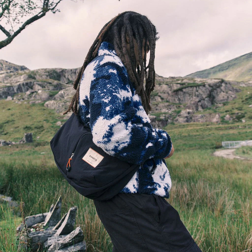 Person wearing a blue and white tie-dye jacket with a black backpack in a natural landscape.