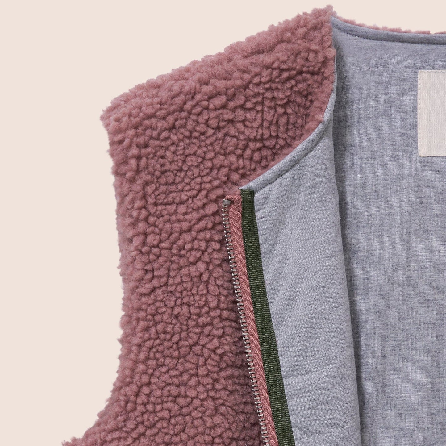 Close-up of a pink fleece vest with a gray interior on a beige background