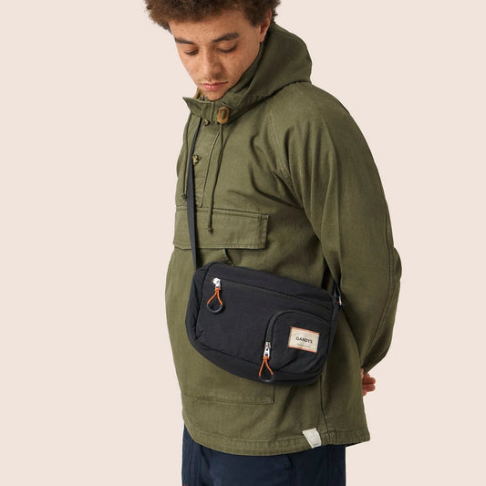 Person wearing an olive green jacket with a navy sling bag on a beige background