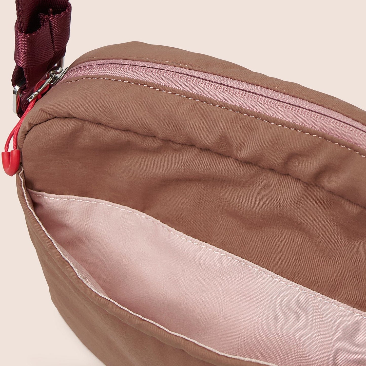 Close-up of a brown bag with a red zipper on a beige background