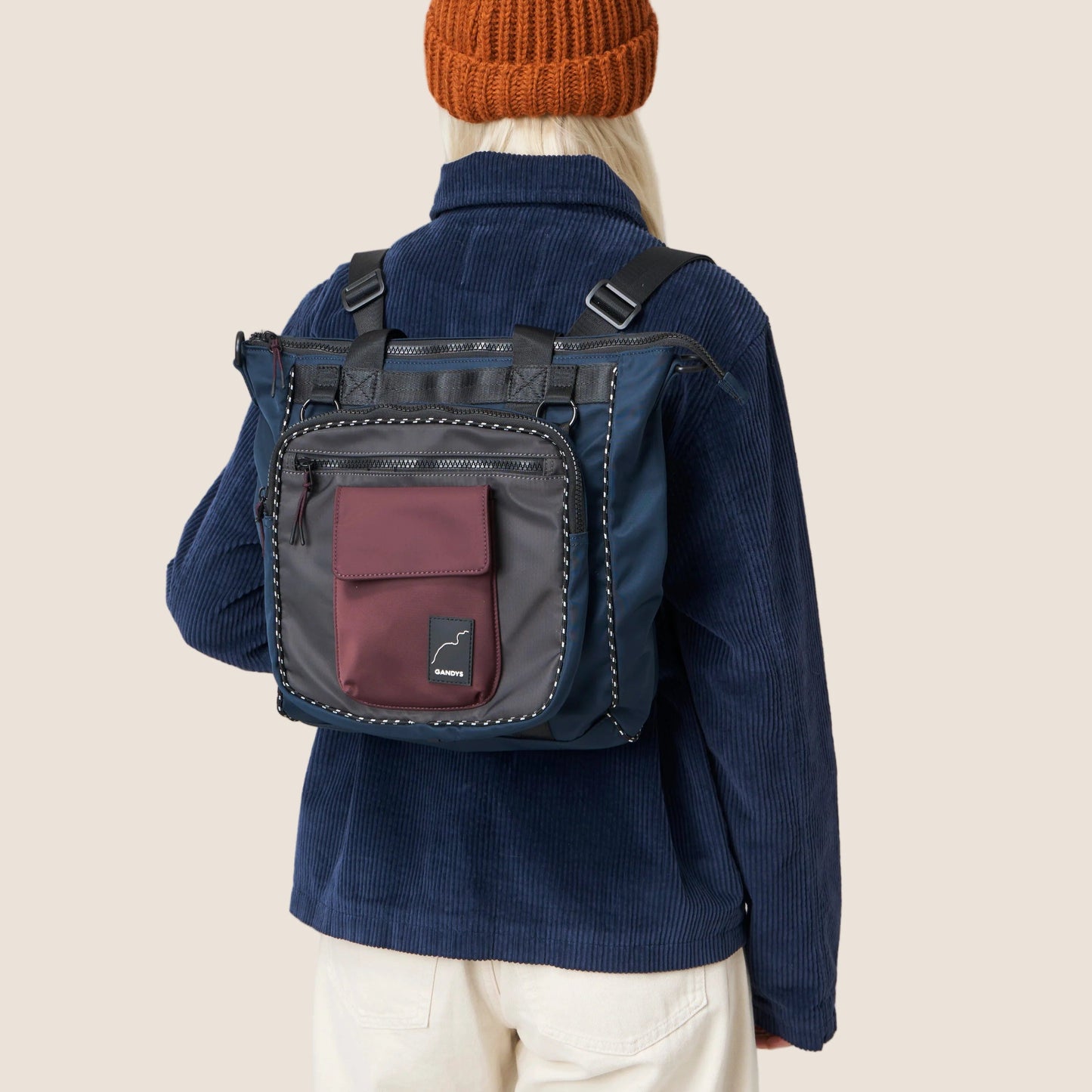 Person wearing a blue jacket with a black backpack on a beige background