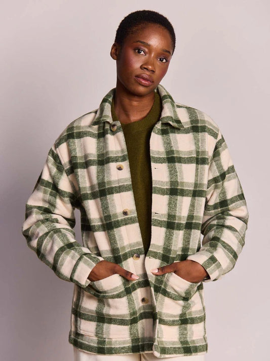 A model wearing a green and cream plaid button-up flannel shirt jacket over an olive green top, photographed against a neutral light gray studio background.