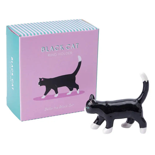 A black ceramic cat-shaped ring holder with a white belly, positioned in front of its pink gift box with vertical blue stripes.