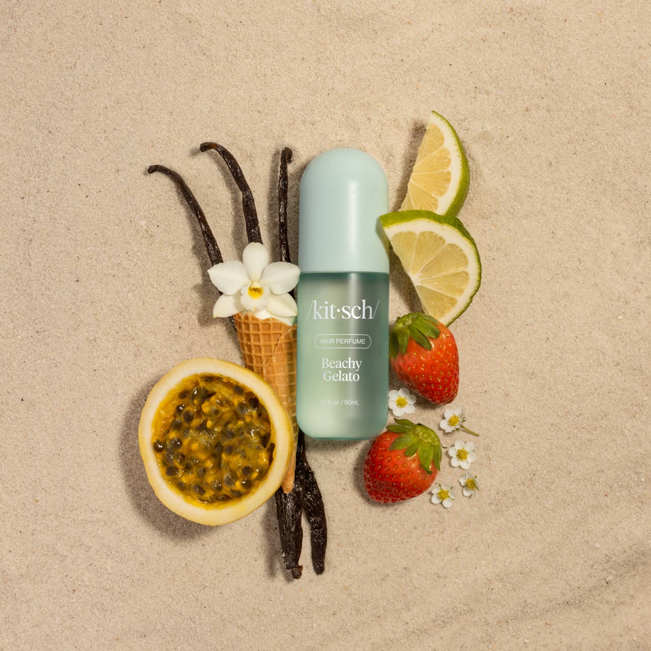 Beachy Gelato Hair Perfume on sand with scent inspired objects around the bottle, such as strawberry, lime and vanilla 