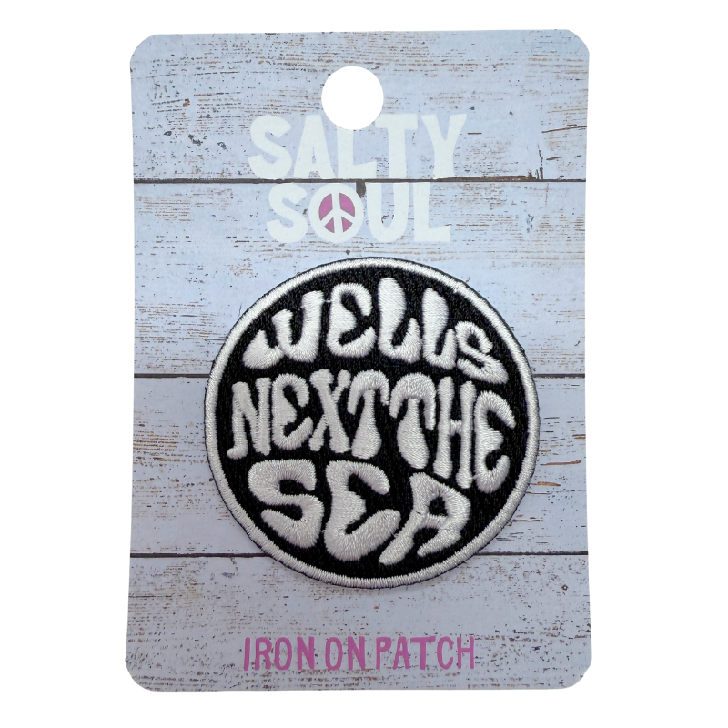 Embroidered  Iron-on patch with 'Wells Next The Sea' text in black and white on a wooden textured card with 'Salty Soul' branding.