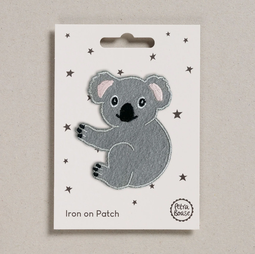 Embroidered iron on Grey Koala patch, on a white card with black stars and 'Petra Boase' Branding 