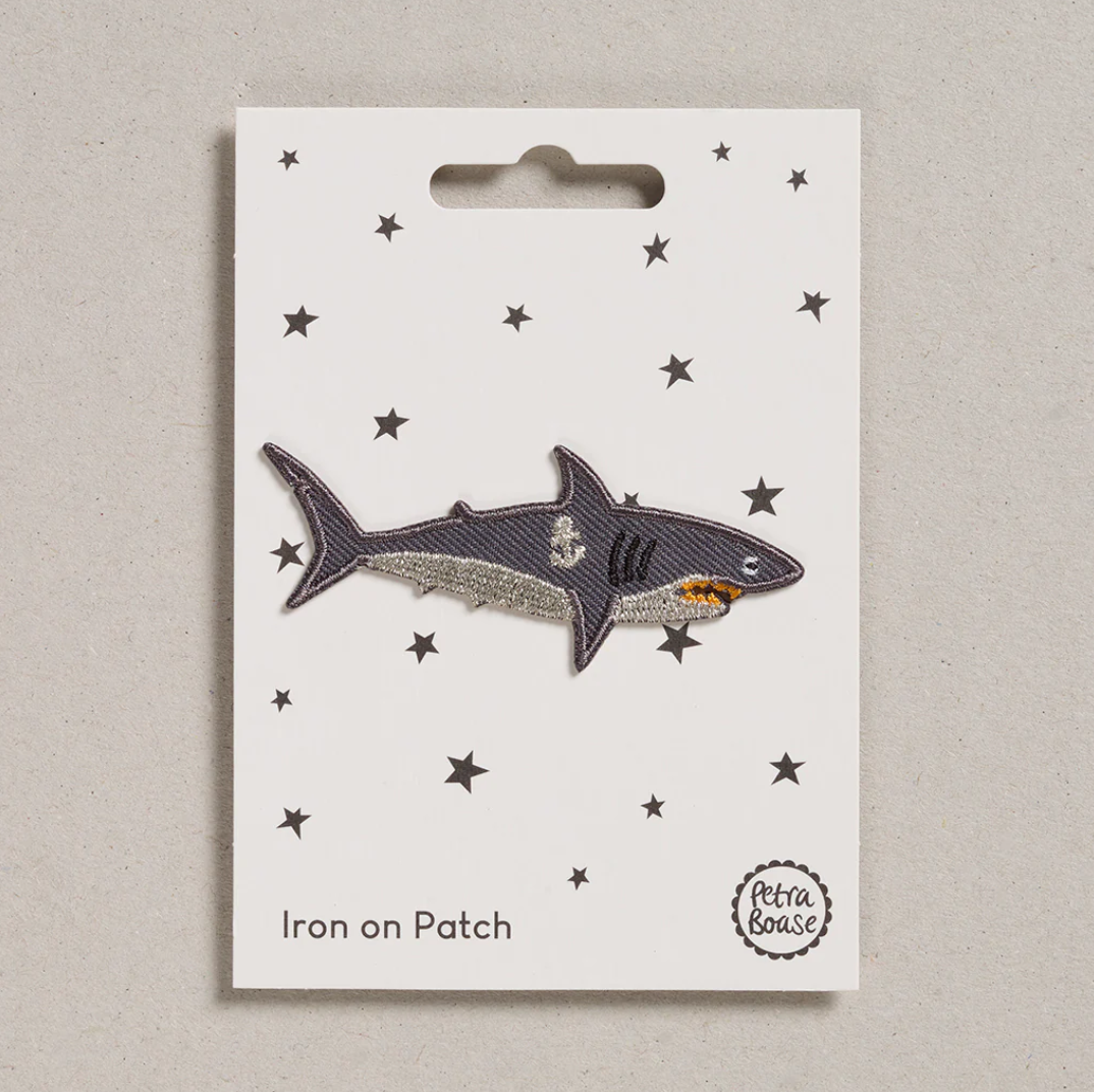 Embroidered iron on Shark patch, on a white card with black stars and 'Petra Boase' Branding 