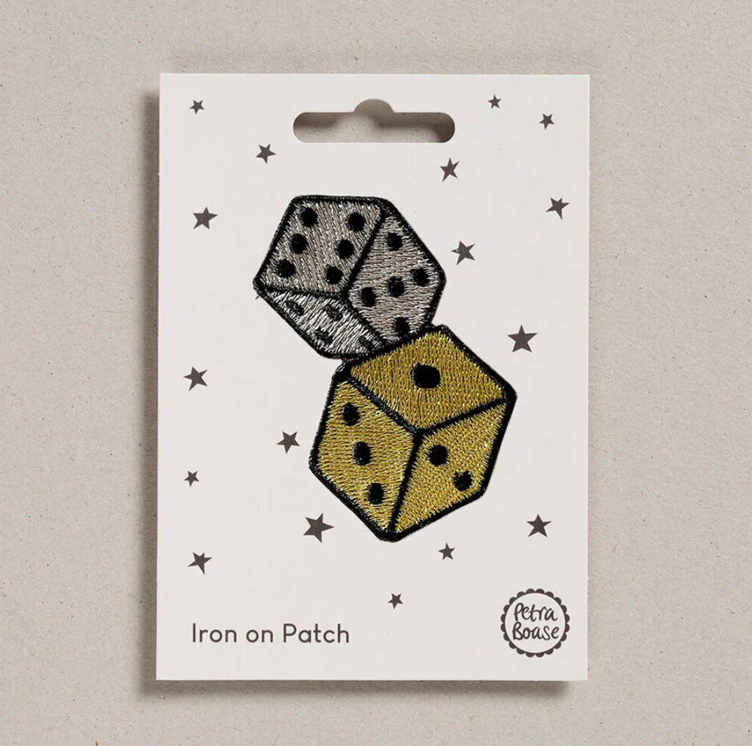 Embroidered iron on metallic rolled dice patch, on a white card with black stars and 'Petra Boase' Branding 