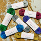 seven rolls of glitter shoes laces, in various colours, wrapped in a glitter and mud branded label on a wooden background.
