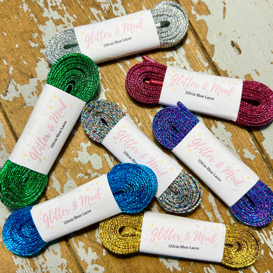 seven rolls of glitter shoes laces, in various colours, wrapped in a glitter and mud branded label on a wooden background.