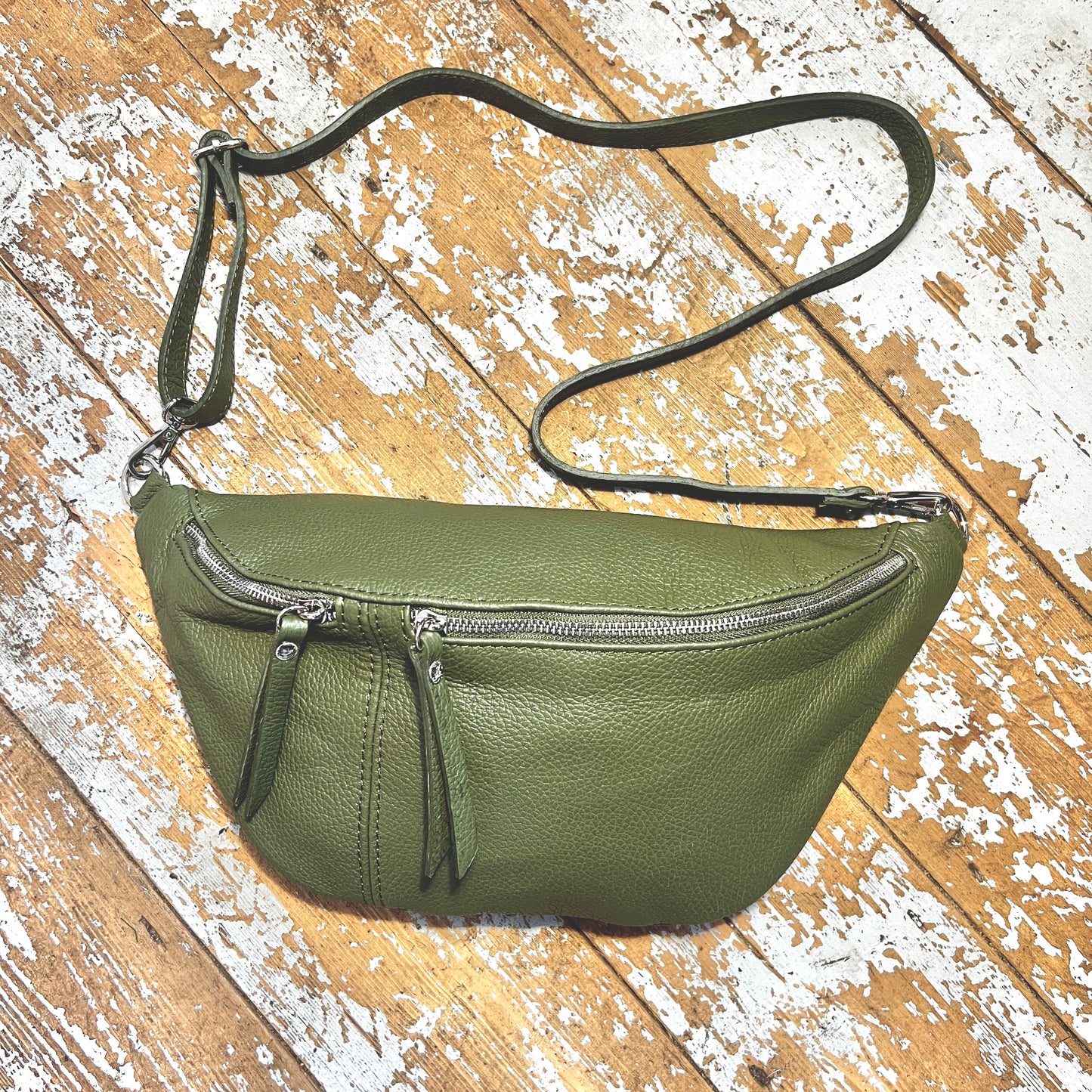 Khaki green XL leather bum bag with silver hardwear on a wooden surface 