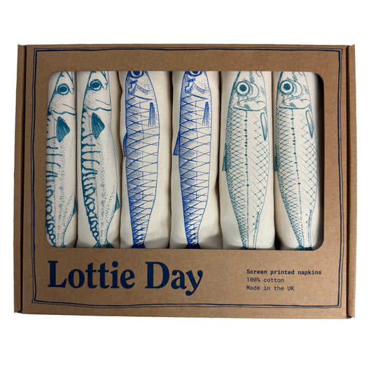 Box of screen printed napkins with fish design by Lottie Day on a wooden surface.