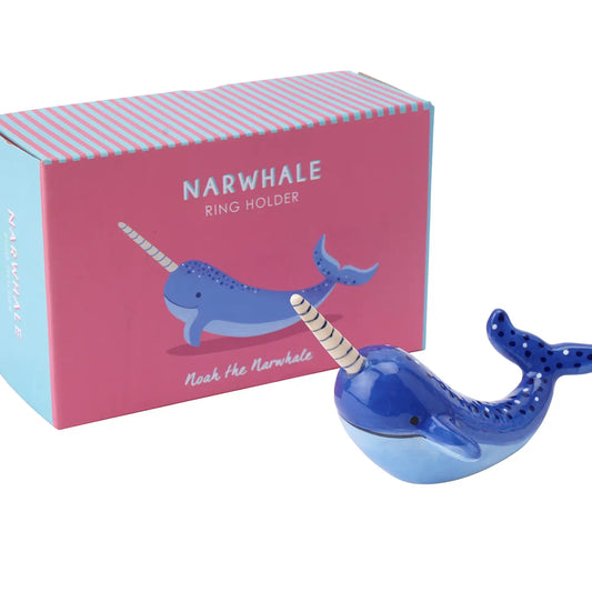A Narwhale ceramic ring holder r with a blue belly, positioned in front of its pink gift box with vertical blue stripes.