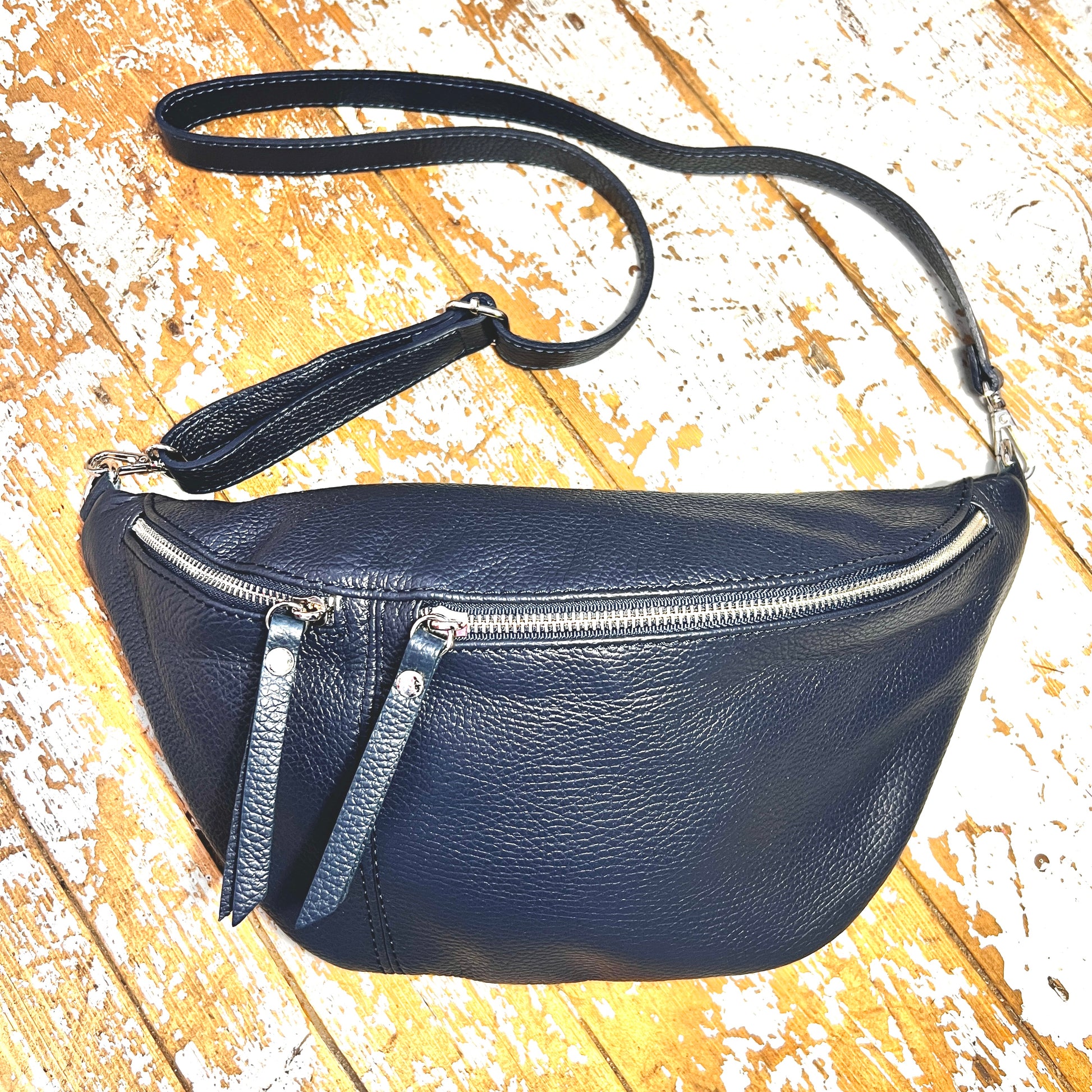 Navy XL leather bum bag with silver hardwear and detachable strap on a wooden surface 