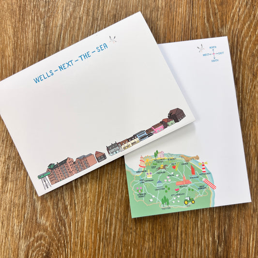 Two note pads on a wooden surface, one with wells next-the sea Quay illustrated buildings and the other with a map of the North Norfolk coast .