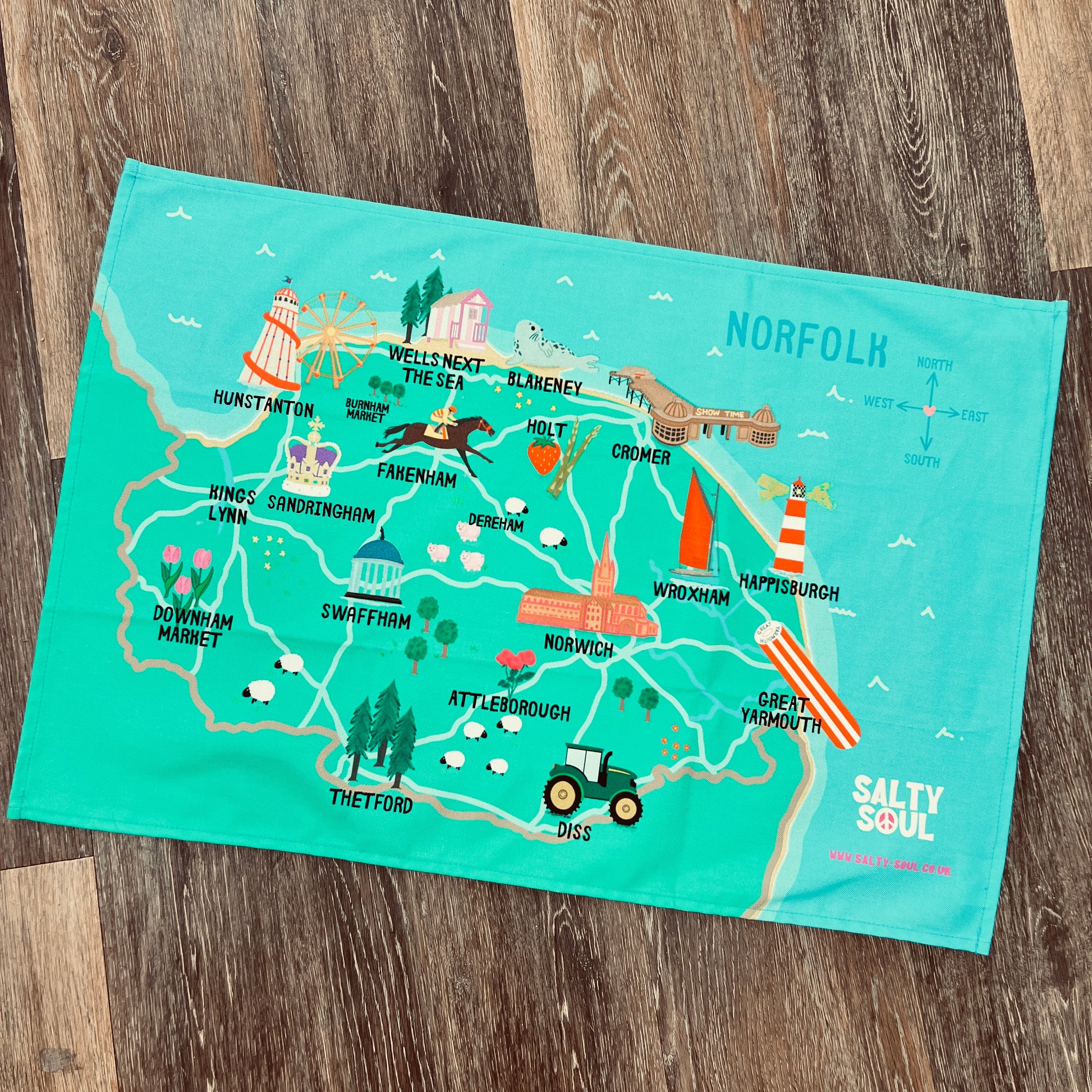 Map of the North Norfolk area on a teal tea towel with 'Salty Soul' branding, placed on a wooden surface.