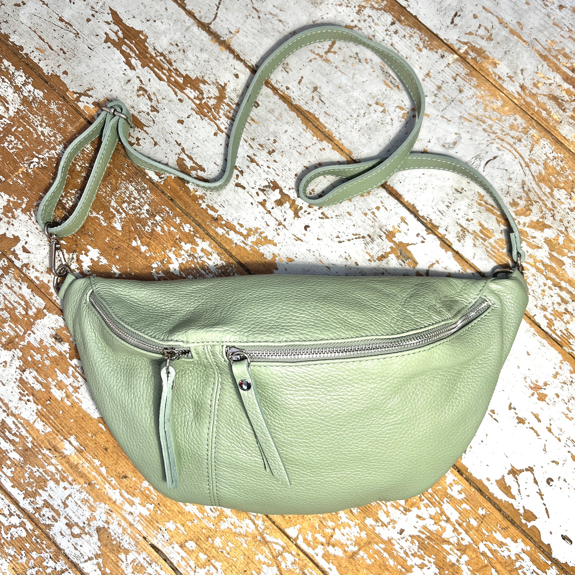 Pastel green XL leather bum bag with silver hardwear and detachable strap on a wooden surface 