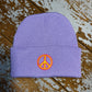 Pastel Lilac beanie hat with embroidered peace sign on cuff , laid out on a wooden surface.