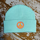 Pastel beanie hat with embroidered peace sign on cuff , laid out on a wooden surface.