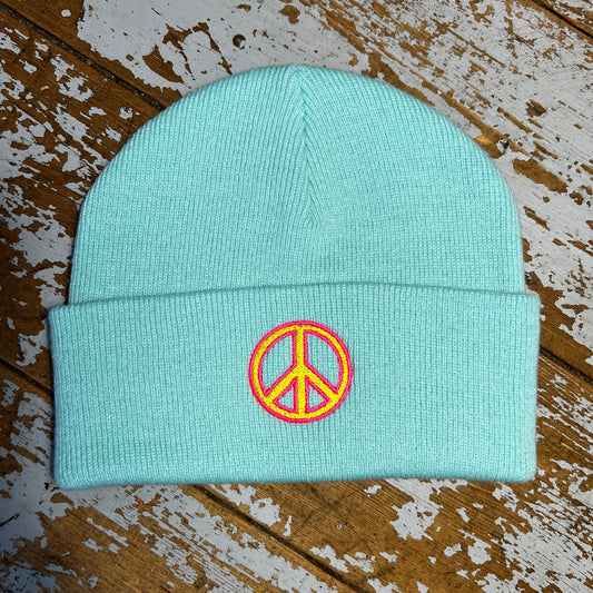 Pastel beanie hat with embroidered peace sign on cuff , laid out on a wooden surface.
