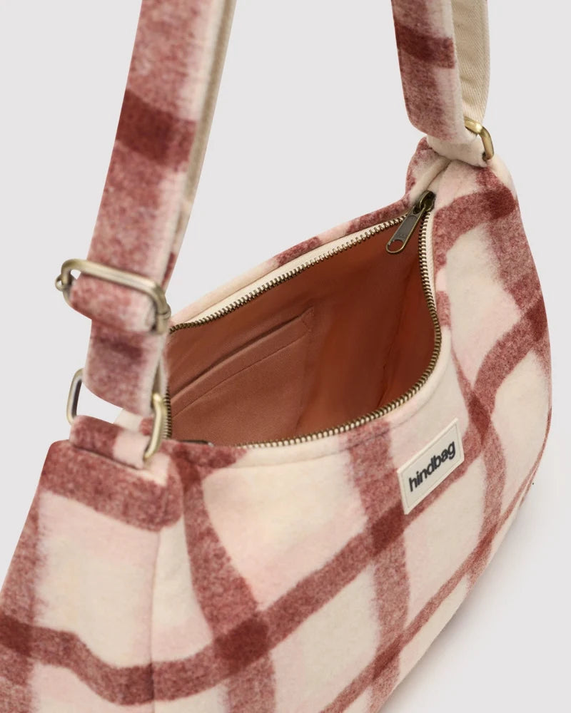 A close-up of a soft, fuzzy shoulder bag with a dusty pink and white plaid pattern, featuring a gold zipper and a small white 'handbag' brand label.
