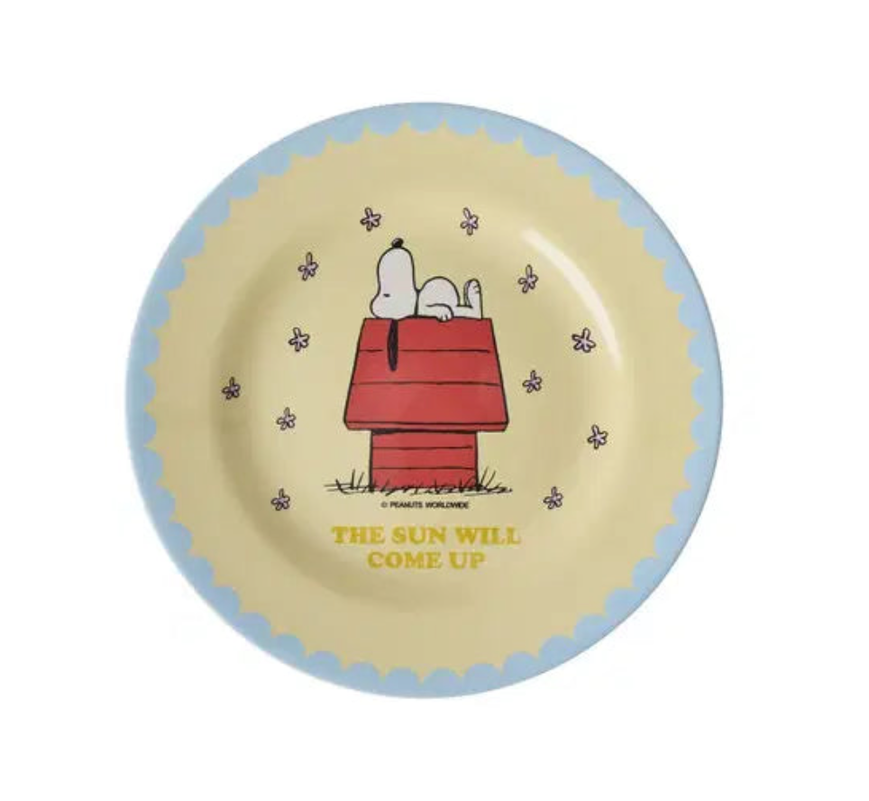 Snoopy pale yellow melamine plate with cartoon snoopy on top of a red dog house. the plate has a scallop blue edge n a white background.