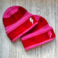 Two Red and pink stripped beanies with pink and silver embroidered bolts on a wooden background 