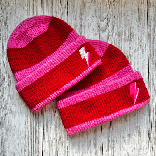 Two Red and pink stripped beanies with pink and silver embroidered bolts on a wooden background 
