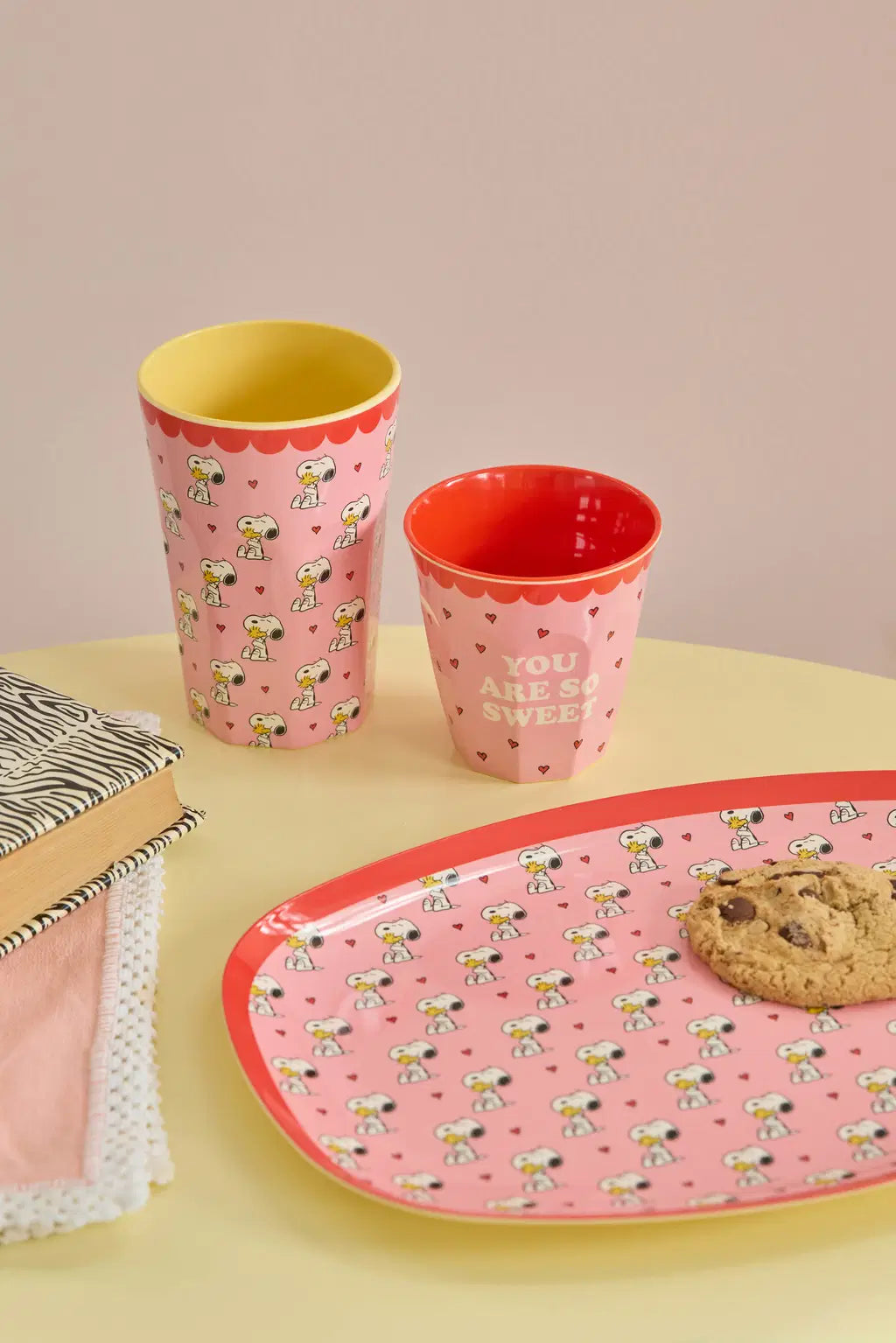 Two patterned cups and a matching tray on a yellow surface with a pink background.