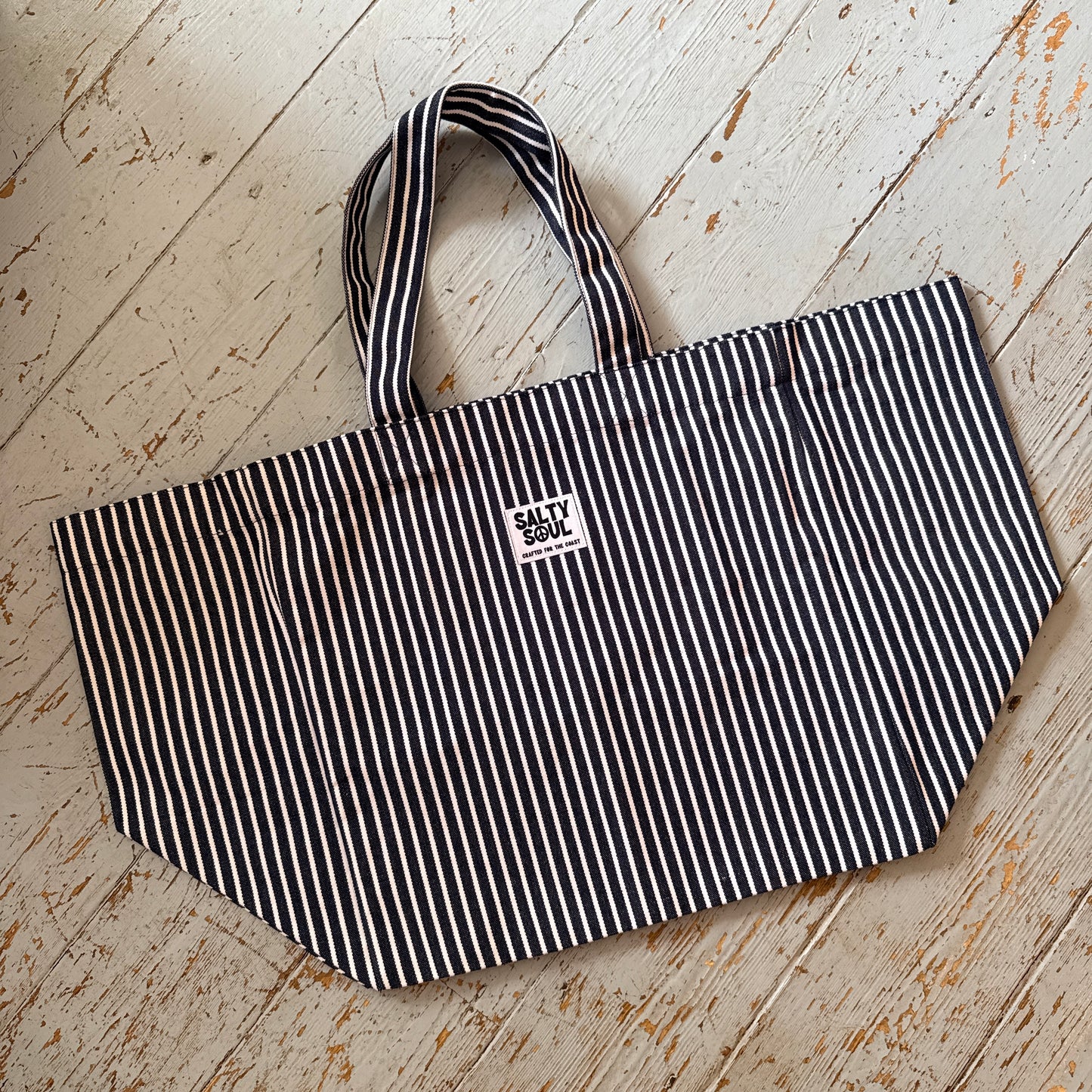 Large black and white striped tote bag with a white salty soul label on the front, on a wooden floor.
