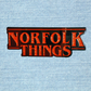 Red Glitter enamel pin badge  'Norfolk Things' text on a denim background