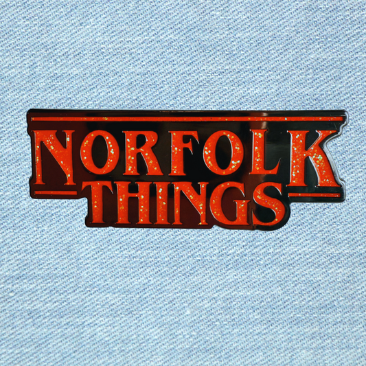Red Glitter enamel pin badge  'Norfolk Things' text on a denim background