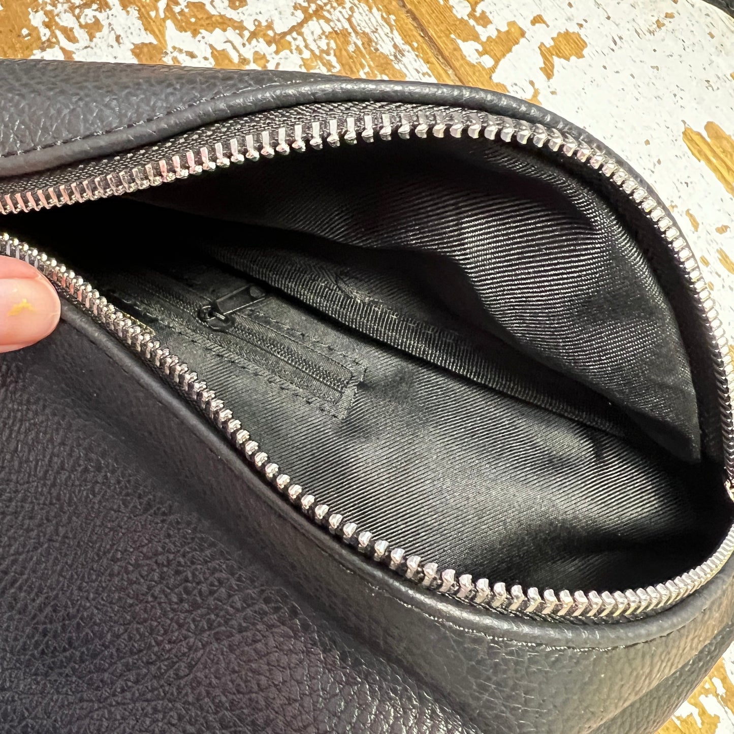 black leather XL bum bag showing silver zip opening and inside black zip within bag, on a wooden surface 