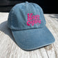 blue dad cap with pink embroidered 'Happy Camper' in fun lettering, on w light wooden background 