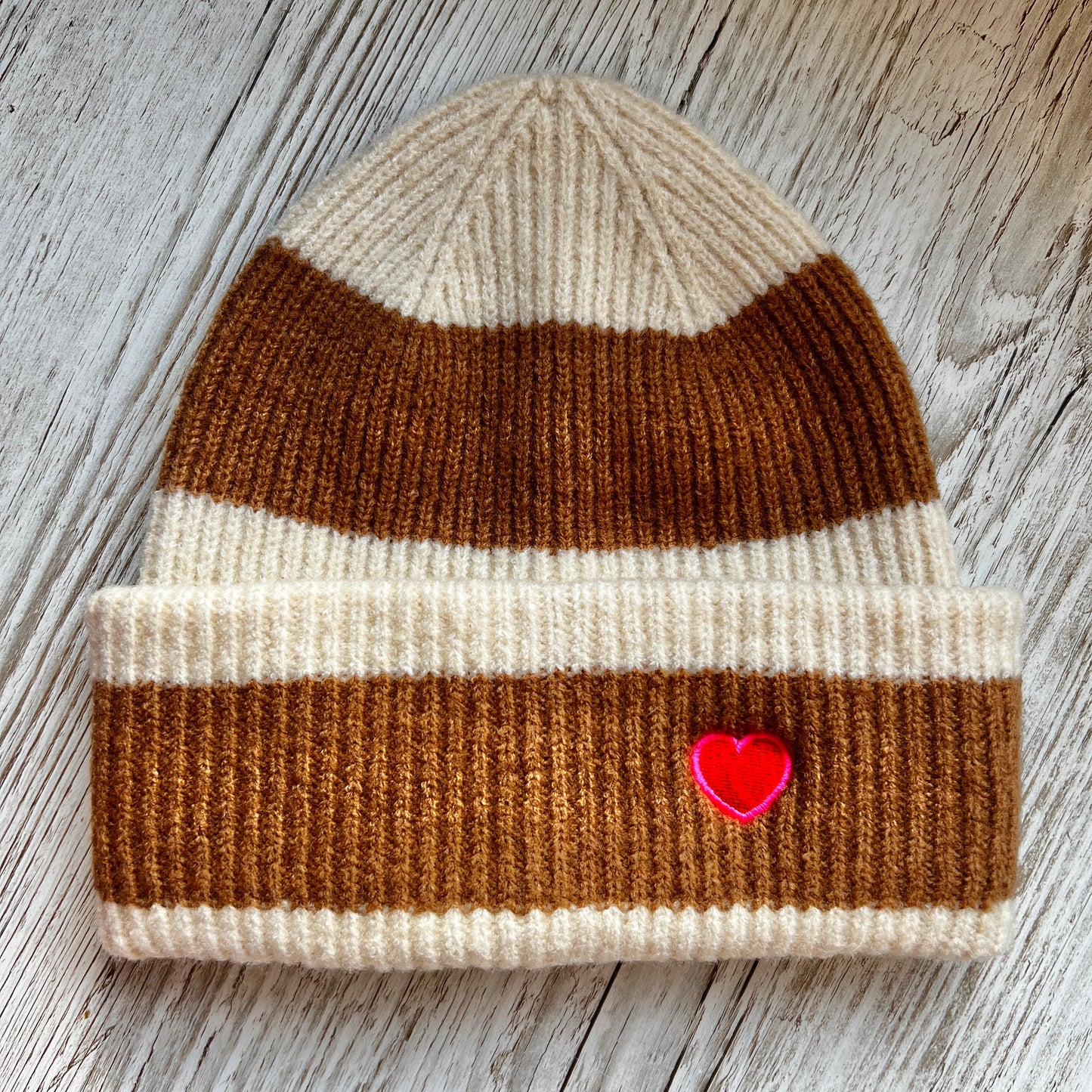 brown and beige striped beanie with an embroidered red and pink heart on a wooden background 