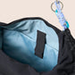 Gandys black bag with blue interior and a keychain attached, on a beige background