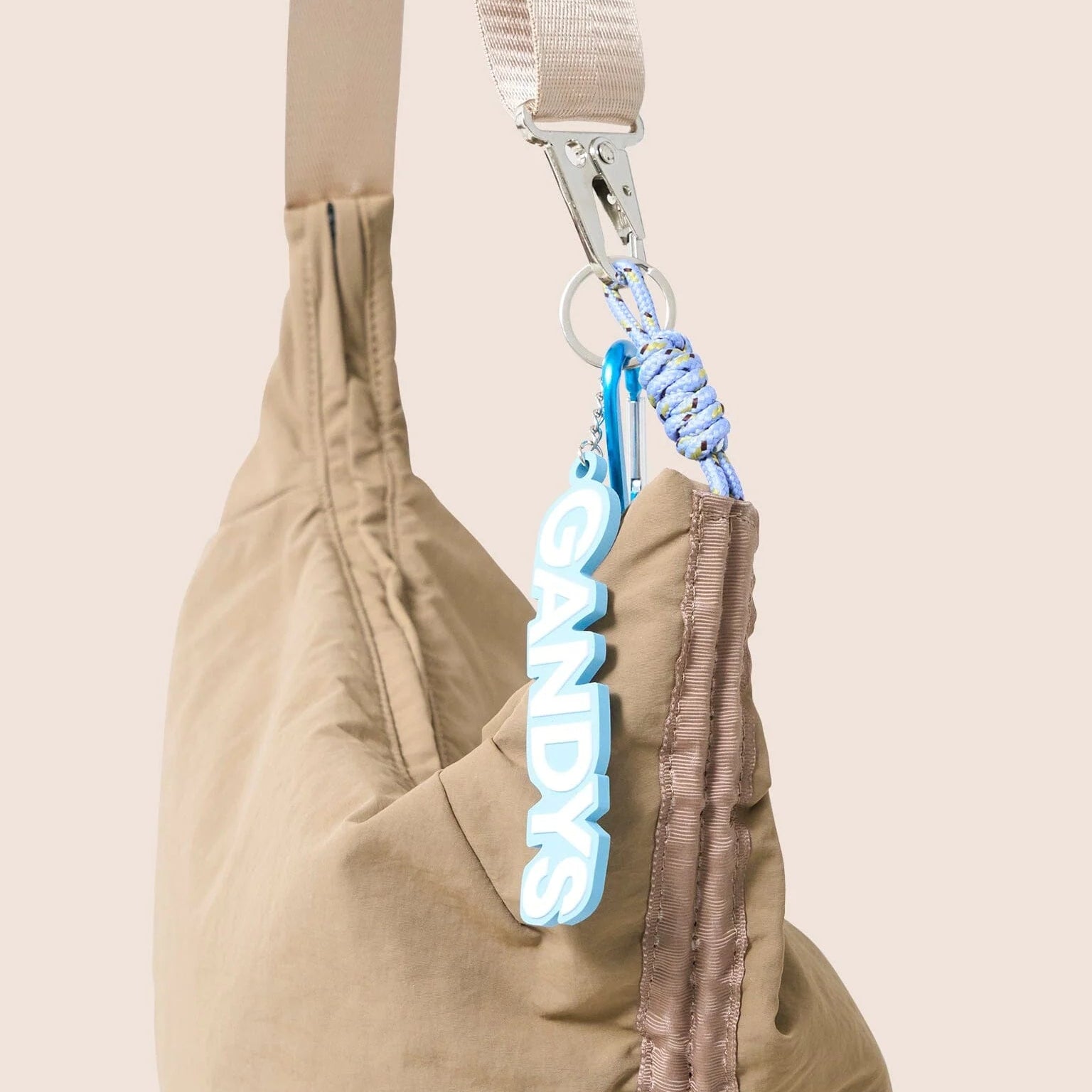 Gandys taupe bag with a blue and white carabiner attached on a beige background