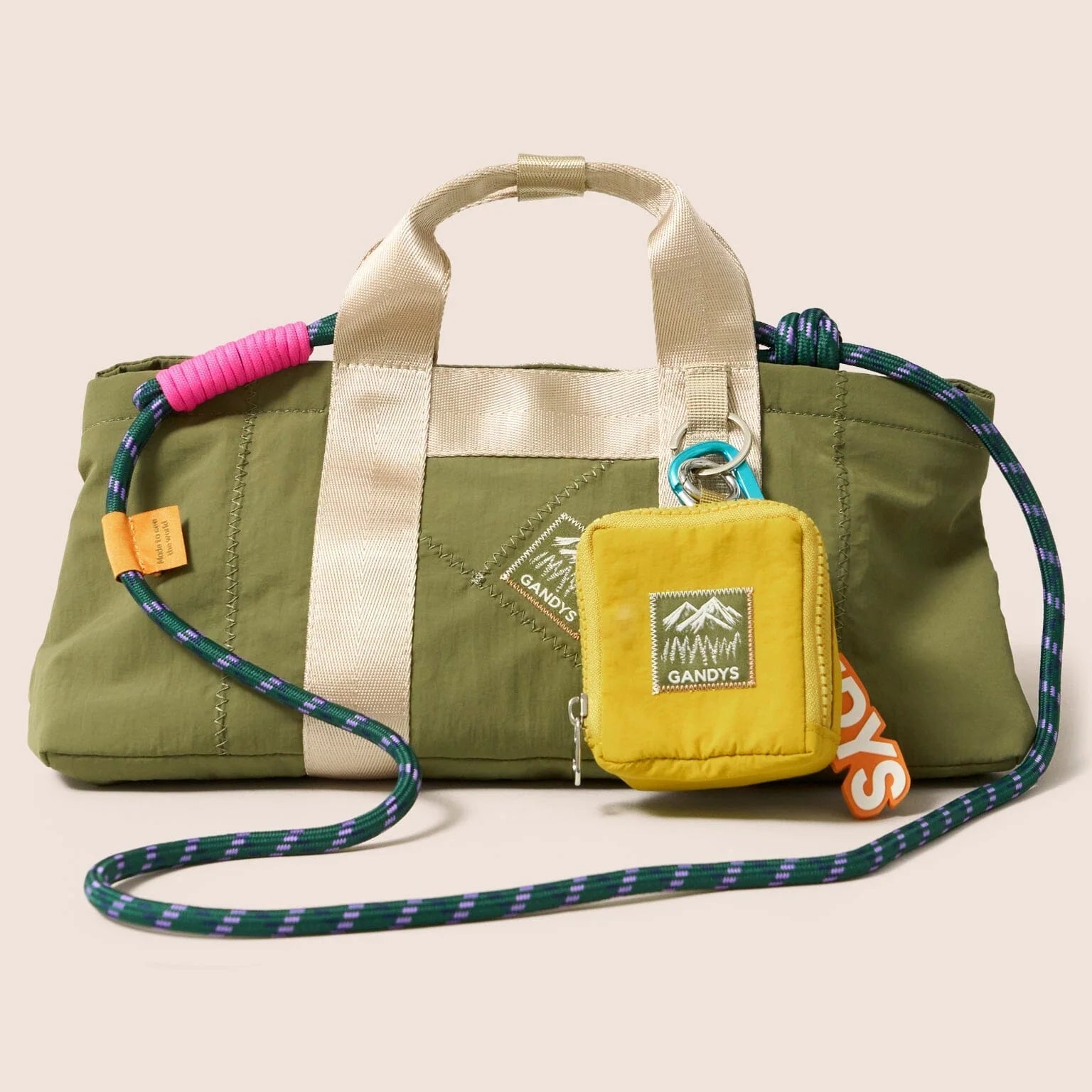 Green duffel bag with a yellow pouch and colorful strap on a beige background