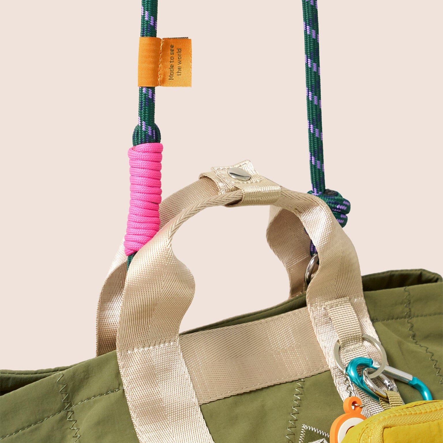 Close-up of a green bag with colorful handles and a beige strap on a beige background