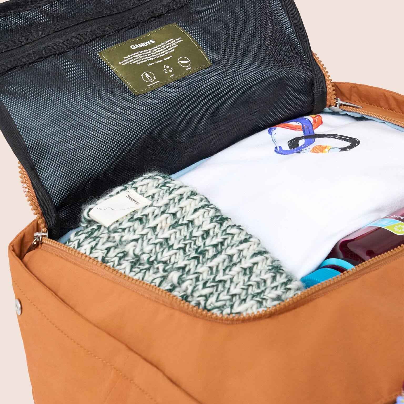 Open borange travel bag with clothes and items on a beige background