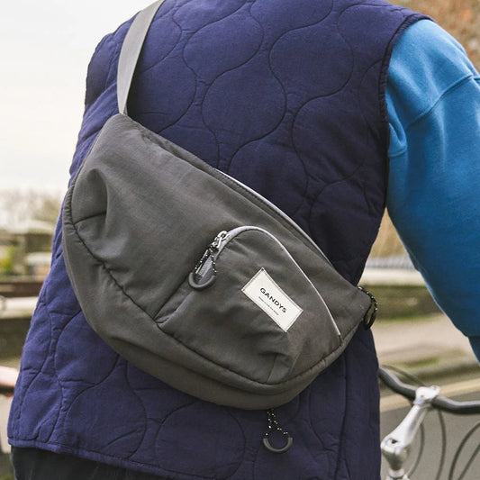 Person wearing a dark blue quilted vest with a gray crossbody bag, standing outdoors.