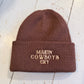 Brown beanie with embroidered  'MAKIN COWBOYS CRY' text on a wooden surface