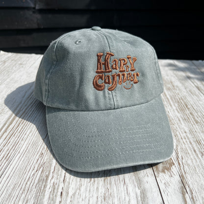 grey wash denim dad cap with brown embroidered 'happy camper' text onn a light coloured wooden surface  
