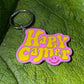 pink and yellow enamel 'Happy Camper' Key ring with a small red smiley face, on a green leaf 