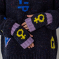 Person wearing dark sweater with colorful symbols and purple and navy fingerless gloves with feminist yellow symbols.
