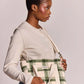 A woman wearing a cream cardigan and blue jeans holds a green and cream plaid tote bag with a shoulder strap. The bag has a small white label that reads 'hindbag'.