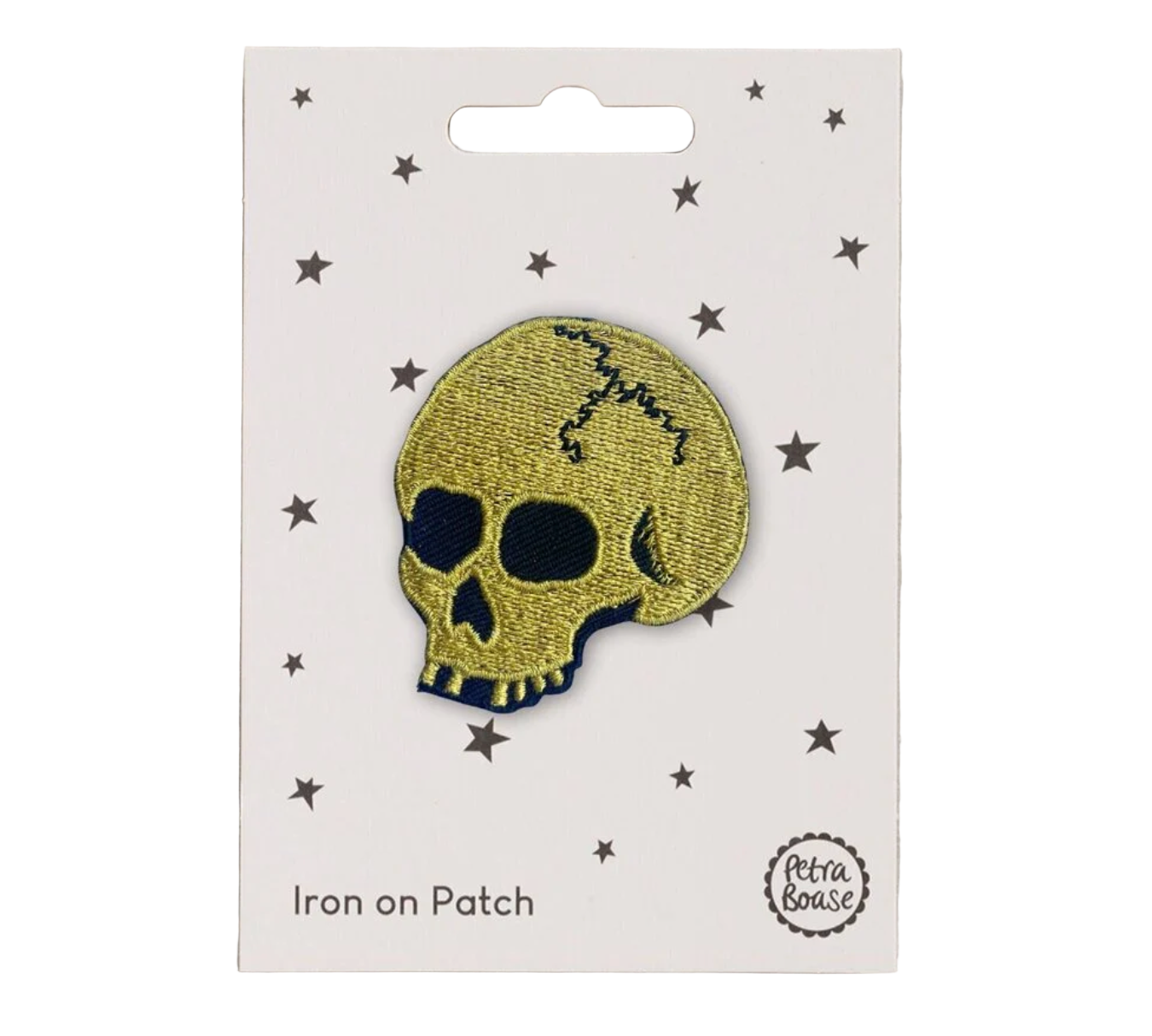 A metallic gold skull patch with iron-on backing, displayed on a card with small stars around it Petra Boase branding