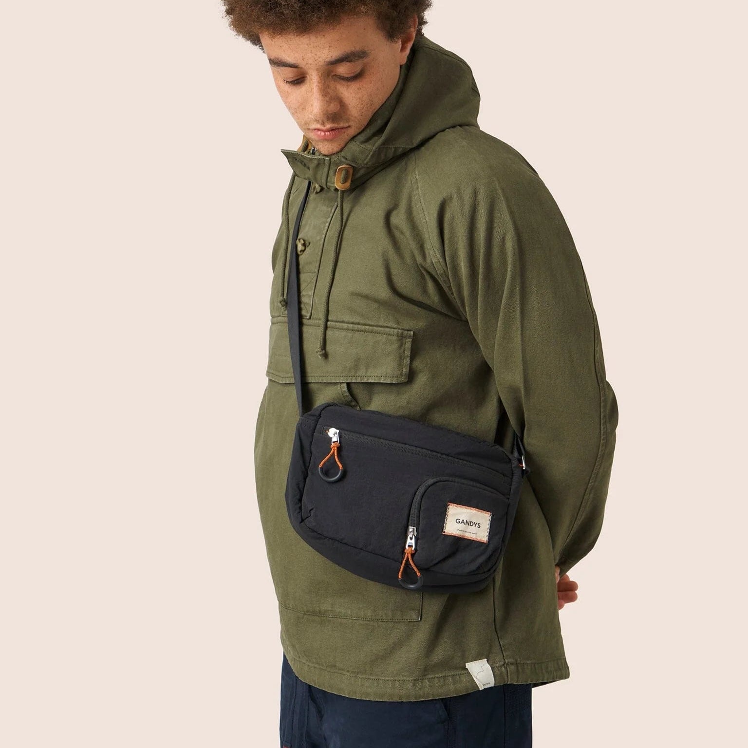 Person wearing an olive green jacket with a navy sling bag on a beige background