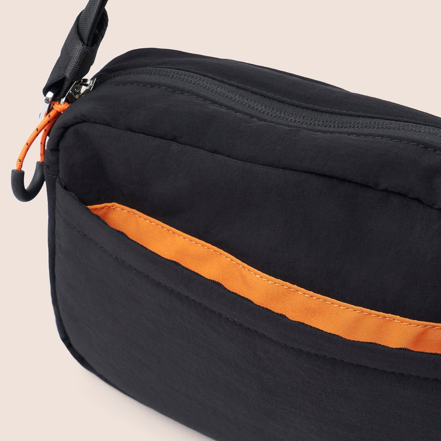 Black bag with orange interior lining on a beige background